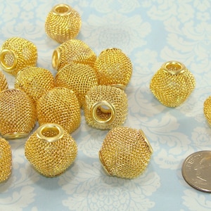 May include: A group of gold-coloured metal beads with a mesh design. The beads are round and have a hole in the centre. They are scattered on a light blue background with a floral pattern.
