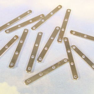 May include: A group of silver metal connector straps with four holes each. The straps are scattered on a white surface.