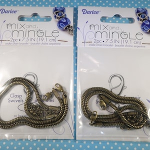 May include: Two packages of Darice snake chain bracelets. Each bracelet is 7.5 inches (19.1 cm) long and has a clasp and swivels. The packaging includes the text "mix and mingle". The bracelets are a bronze color.