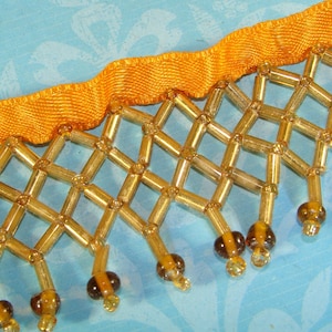 May include: Gold and brown beaded trim with a yellow satin ribbon. The trim features a diamond pattern with dangling beads.