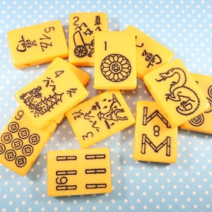 May include: A set of yellow mahjong tiles with black Chinese characters and symbols. The tiles feature numbers, characters, and symbols.