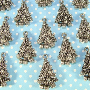 Puede incluir: Una colecci&oacute;n de dijes de &aacute;rbol de Navidad plateados con un dise&ntilde;o detallado. Los dijes est&aacute;n dispuestos sobre un fondo azul con lunares blancos.
