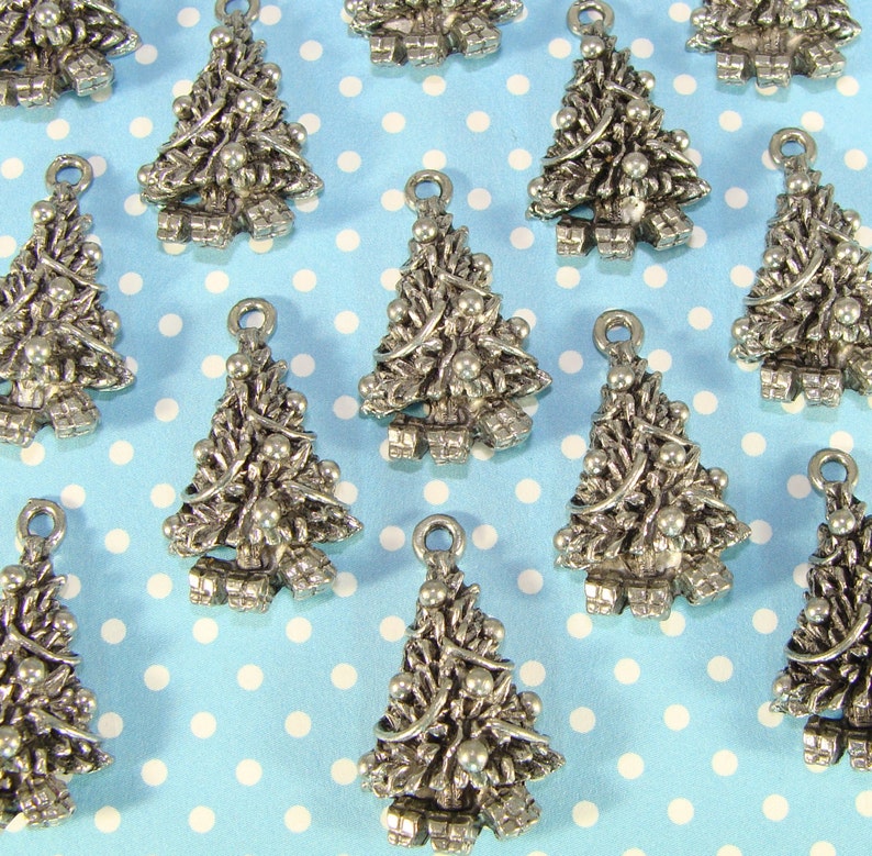 Puede incluir: Una colecci&oacute;n de dijes de &aacute;rbol de Navidad plateados con un dise&ntilde;o detallado. Los dijes est&aacute;n dispuestos sobre un fondo azul con lunares blancos.