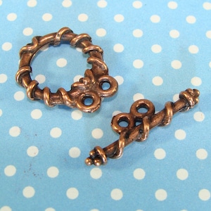May include: Two antique copper-toned metal clasps with a twisted rope design. One clasp is a circle with a decorative flourish, and the other is a straight bar with two loops.