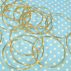 Puede incluir: Un montón de aros de metal dorado, probablemente para la fabricación de joyas, sobre un fondo azul con lunares blancos.