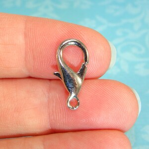 Puede incluir: Cierre de langosta de metal plateado con un cierre de resorte. El cierre está diseñado para sujetarse a joyas, bolsos u otros accesorios.