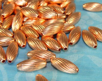 May include: A pile of copper-colored oval beads with a ribbed texture. The beads are scattered on a blue surface.