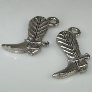 May include: Two silver-toned metal boot charms with a feather design. The boots have a pointed toe and a spur on the heel.