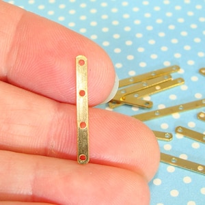 May include: Gold metal connector straps with four holes. The straps are about 1 inch long and are shown in a hand.