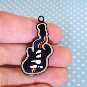 May include: Black guitar-shaped charm with a rainbow design and white text. The charm has a small loop at the top for attaching to a necklace or bracelet. The guitar design features a rainbow of colours and a white question mark.