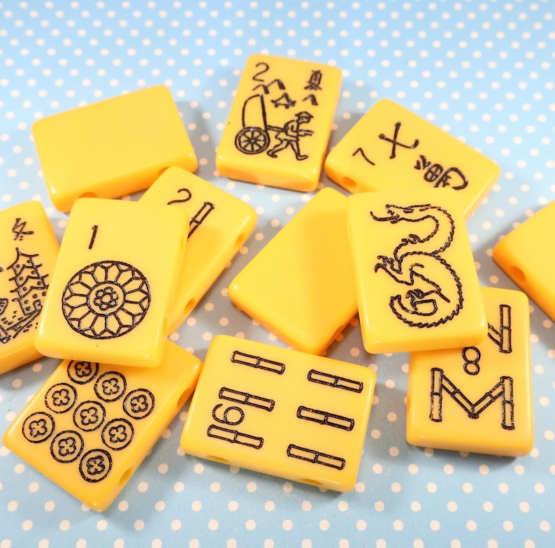 May include: A set of yellow plastic mahjong tiles with black markings. The tiles feature various symbols and numbers, including a dragon, bamboo, and circles.