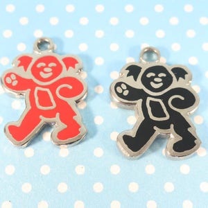 May include: Two metal charms in the shape of a walking bear. One is red with a silver outline, and the other is black with a silver outline. Both have a loop at the top for attaching to jewelry or other crafts.