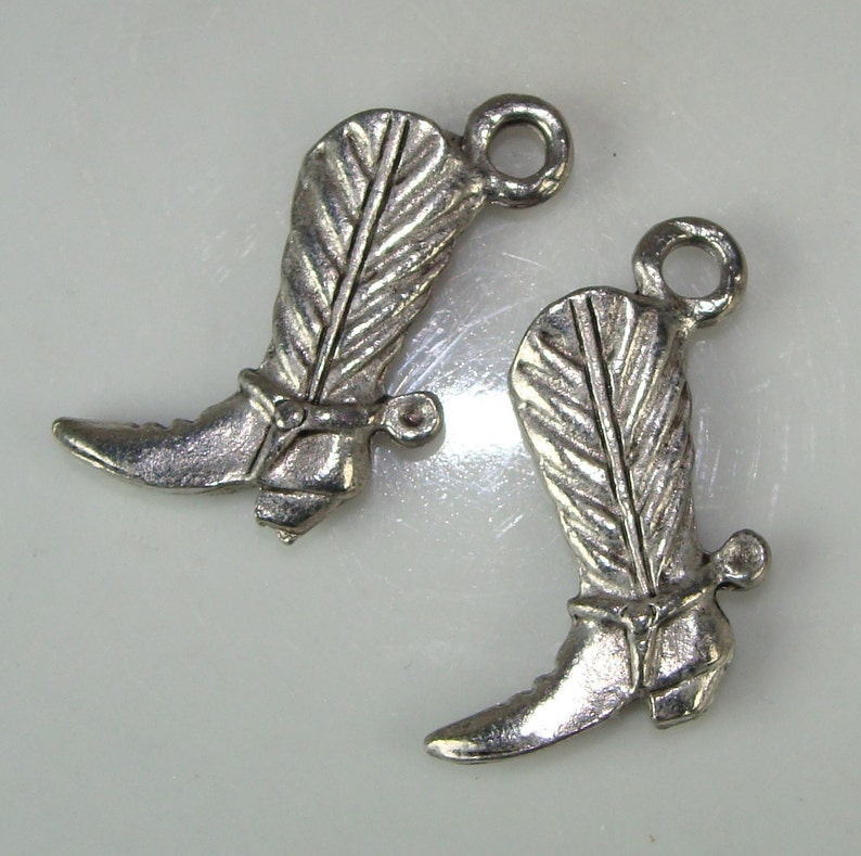 May include: Two silver cowboy boot charms with a feather design and a spur on the heel.