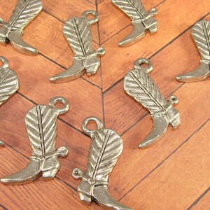 May include: A set of ten silver-toned metal cowboy boot charms. The charms are detailed with a feather design and a spur on the heel.