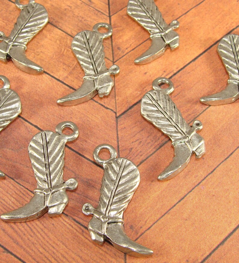 May include: A set of ten silver-toned metal cowboy boot charms. The charms are detailed with a feather design and a spur on the heel.