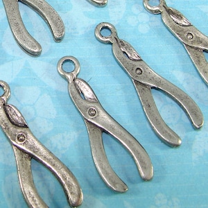 Peut inclure: Un ensemble de six breloques en forme de pinces métalliques argentées. Les breloques mesurent environ 5 cm de long et ont une boucle en haut pour les attacher à un collier ou un bracelet.