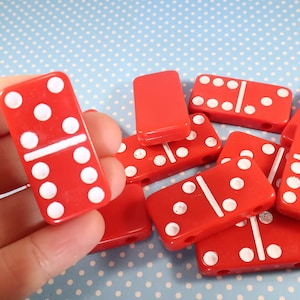 May include: A set of red dominoes with white dots. The dominoes are arranged in a pile, with some of them overlapping. The dominoes are made of plastic and have a smooth, glossy finish.