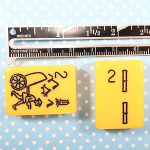 May include: Two yellow mahjong tiles. The first tile has a black illustration of a person carrying a wheelbarrow. The second tile has the number "2" and two vertical black lines.