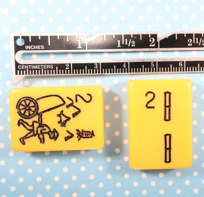May include: Two yellow mahjong tiles. The first tile has a black illustration of a person carrying a wheelbarrow. The second tile has the number "2" and two vertical black lines.