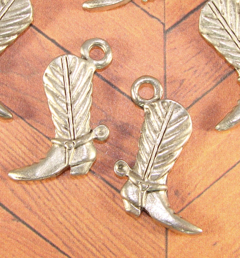 May include: Silver tone metal cowboy boot charms with a feather design and a spur. The charms have a loop at the top for attaching to a necklace, bracelet, or other jewelry.