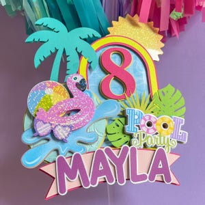 May include: A vibrant cake topper with a pool party theme, featuring a pink flamingo, palm tree, and the number 8. The design includes the words "Pool Party" and the name "Mayla". The topper uses bright colours and glitter details.