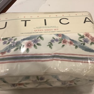 Peut inclure: Un ensemble de draps Queen emballé par Utica. L'ensemble de draps est blanc avec un motif floral rose, violet et vert. L'emballage indique "NO IRON PERCALE" et comprend deux taies d'oreiller, un drap plat et un drap-housse.