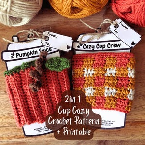 May include: Two crochet cup cozies, one resembling a pumpkin with a stem and leaf, the other with a checkered pattern. Each cozy is attached to a paper cup-shaped tag with the text "Pumpkin Spice" and "Cozy Cup Crew". The image also includes yarn.