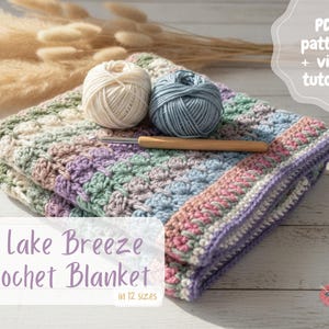 May include: A folded crochet blanket featuring a multi-coloured pastel striped pattern in shades of pink, blue, green, and cream. Two yarn balls in cream and blue sit on top with a wooden crochet hook. Text reads: PDF pattern + video tutorial, Lake Breeze Crochet Blanket in 12 sizes.
