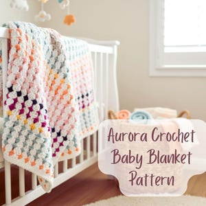 Può includere: Una coperta per neonati all'uncinetto fatta a mano in una culla. La coperta presenta un motivo a granny square in bianco, rosa, arancione e viola. Il testo sull'immagine recita "Aurora Crochet Baby Blanket Pattern".