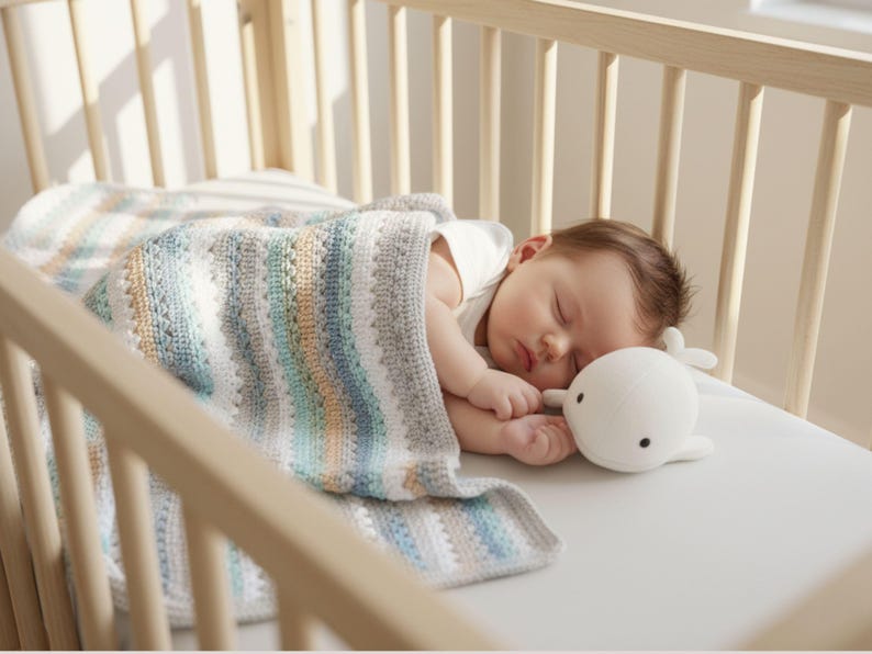 May include: A sleeping baby in a wooden crib, covered with a striped, multi-colored blanket. A white whale-shaped plush toy rests beside the baby. The blanket features stripes of blue, gray, and tan.