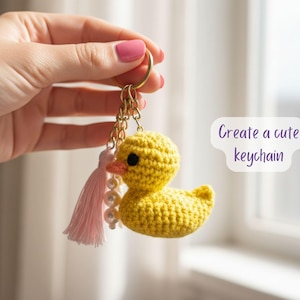 Pu&ograve; includere: Un portachiavi a forma di anatra gialla all'uncinetto fatto a mano con occhi neri e becco arancione. Il portachiavi ha una catena color oro, un nappa rosa e una fila di perle. Il testo sull'immagine recita "Create a cute keychain."