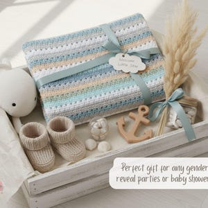May include: A baby gift set in a white wooden crate. The set includes a crocheted blanket with blue, gray, and tan stripes, a plush whale, baby booties, a wooden anchor, and decorative elements. A ribbon and tag that says "Welcome Little Star" adorn the blanket.