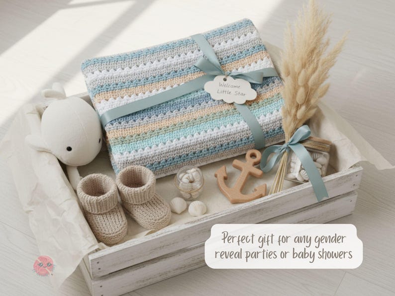 May include: A baby gift set in a white wooden crate. The set includes a crocheted blanket with blue, gray, and tan stripes, a plush whale, baby booties, a wooden anchor, and decorative elements. A ribbon and tag that says "Welcome Little Star" adorn the blanket.