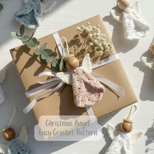 May include: Crocheted angel ornaments in white, pink, and green with wooden bead heads and white wings. A wrapped gift with a white ribbon and dried flowers is in the center. The text "Christmas Angel Easy Crochet Pattern" is visible.