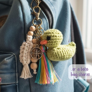 Pu&ograve; includere: Un portachiavi fatto a mano con un'anatra verde all'uncinetto, una nappa colorata, perline di legno e un ciondolo a forma di bussola. Il ciondolo &egrave; attaccato a uno zaino di jeans con un fermaglio di metallo.