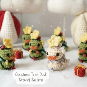 Könnte beinhalten: Gehäkelte Weihnachtsbaum-Enten mit gelben Sternaufsätzen, grünen Körpern und orangefarbenen Schnäbeln. Kleine rote Geschenkboxen und weiße Wollknäuel befinden sich im Hintergrund. Der Text "Christmas Tree Duck Crochet Pattern" steht unten.