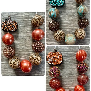 May include: A collection of beaded necklaces featuring pumpkin-shaped pendants and various bead designs. The necklaces showcase a variety of colors and textures, including leopard print, glitter, and iridescent beads. The beads are strung together with a white cord.