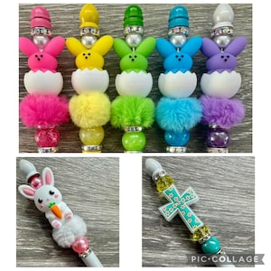 May include: A collection of decorative pens featuring colorful bunny and cross designs. The pens have a variety of colors, including pink, yellow, green, blue, and purple. The bunny pens have fluffy pom-poms and the cross pen has a turquoise cross.