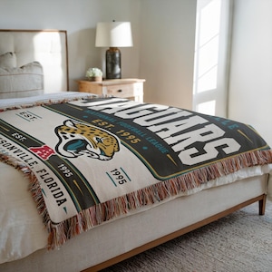 May include: A woven throw blanket featuring the Jacksonville Jaguars logo, the text "JAGUARS", "NATIONAL FOOTBALL LEAGUE", "EST. 1995", and "JACKSONVILLE, FLORIDA". The design includes a jaguar head graphic, teal and gold accents, and fringe edges.