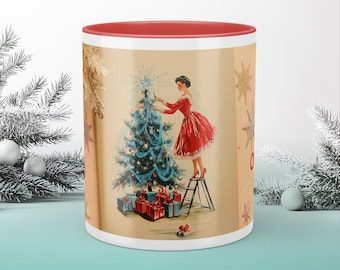 May include: A red and white Christmas mug with a vintage illustration of a woman decorating a Christmas tree. The woman is wearing a red dress and is standing on a ladder. The mug has a red rim and handle.