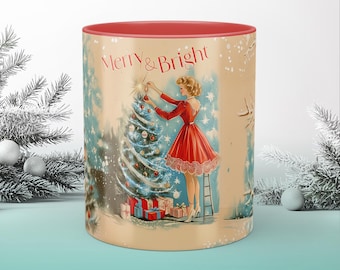 May include: A white ceramic mug with a red rim features a vintage Christmas illustration of a woman decorating a Christmas tree. The text "Merry & Bright" is printed in red on the mug.