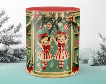 May include: A red and white Christmas mug with a vintage illustration of two girls holding candy canes in front of a decorated window. The girls are wearing red and white striped dresses and have red bows in their hair. The window is decorated with a garland of greenery and ornaments. The mug says "Greetings from the North Pole" on the side.