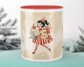 May include: A white ceramic mug with a red rim features a festive illustration of a girl in a red and white striped dress carrying a stack of wrapped gifts. The background is a light beige with a subtle snowflake pattern.