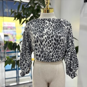 May include: A cropped, long-sleeved top with a black and white leopard print. The top has a round neckline and voluminous sleeves. The garment is displayed on a mannequin with a beige-colored bottom.