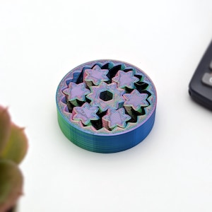 Può includere: Un ingranaggio multi-colorato, stampato in 3D con un design a forma di stella. L'ingranaggio è realizzato in plastica e ha una combinazione di colori blu, verde e viola.