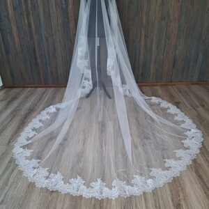 May include: A white tulle wedding veil with a delicate lace trim. The veil is long and flowing, with a scalloped edge.