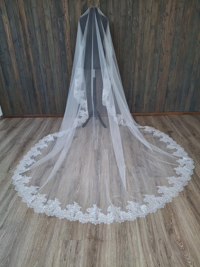 May include: A white tulle wedding veil with a delicate lace trim. The veil is long and flowing, with a scalloped edge.