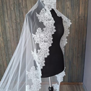 May include: A white bridal veil with a delicate lace trim. The lace features a floral design and is scalloped along the edge.