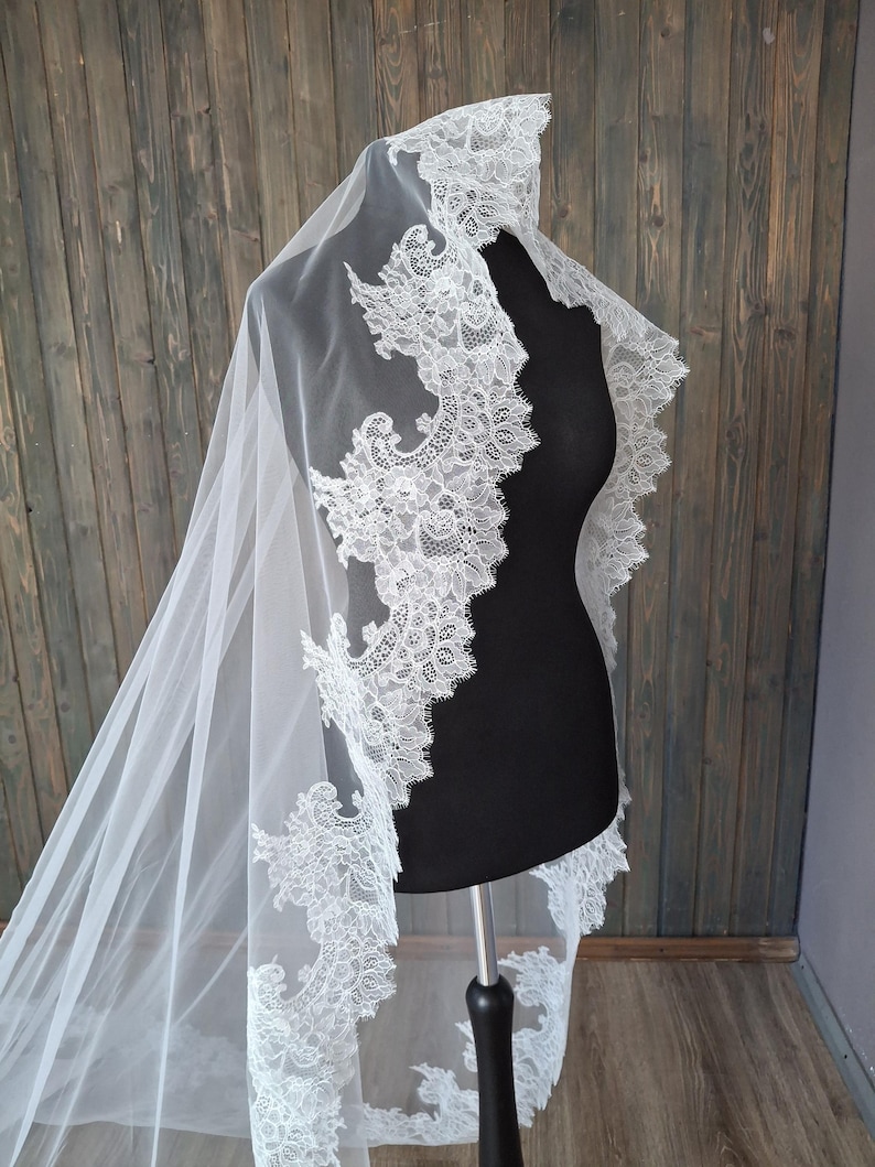 May include: A white bridal veil with a delicate lace trim. The lace features a floral design and is scalloped along the edge.