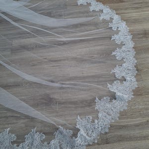 May include: A white bridal veil with a delicate lace trim. The lace is a floral pattern with a scalloped edge.